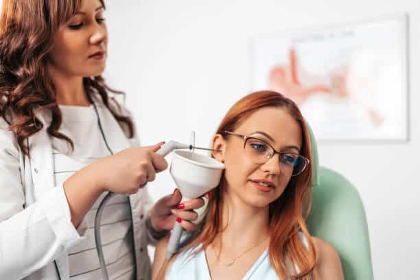 Otolaryngologist doing ear irrigation and earwax removal to a young adult woman with modern medical equipment. Healthcare and medicine concept.